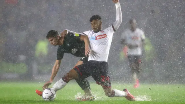 Bolton's Kachunga clashes with Houghton of Plymouth in the torrential rain at Home Park