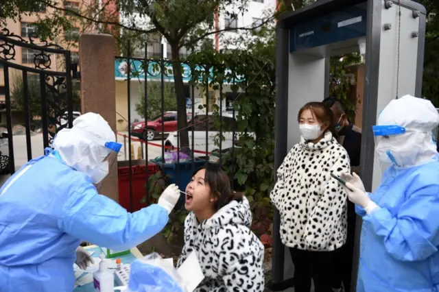 A medical worker in a protective suit collects a swab from a resident in in Lanzhou's Chengguan district, Gansu province.