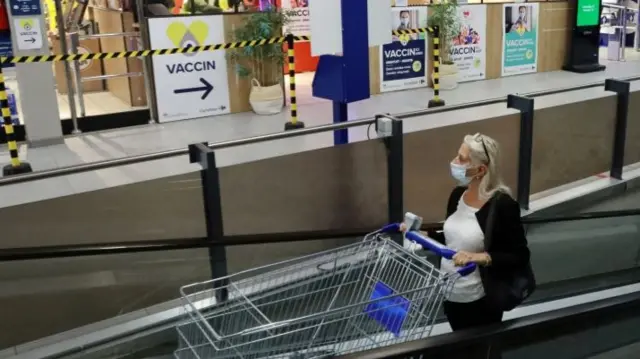 A woman pushes a shopping trolley past a sign for a coronavirus disease (COVID-19) vaccination centre installed inside a supermarket in Brussels, Belgium, August 30, 2021