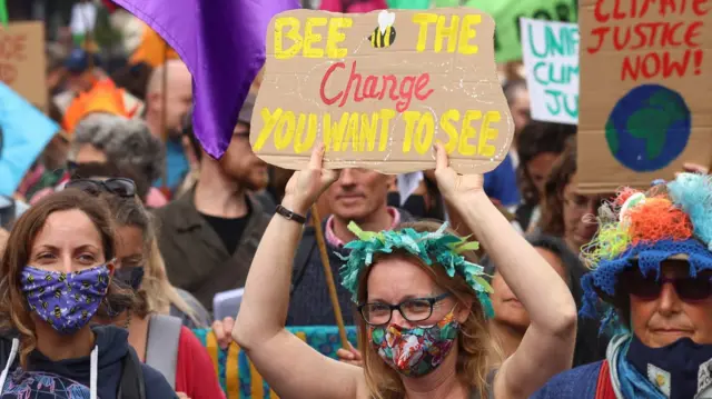 A woman holds up a sign decorated with a bumblebee saying: "Bee the change you want to see"