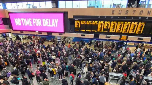 People waiting at Euston under a COP26 sign which says "No time for delay"