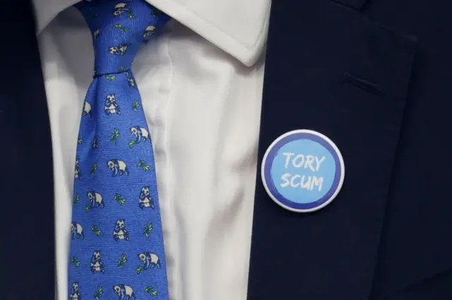 Man in suit wearing badge that reads 'Tory scum'