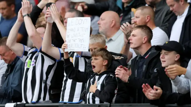 Young Newcastle fan holds up sign protesting against Mike Ashley