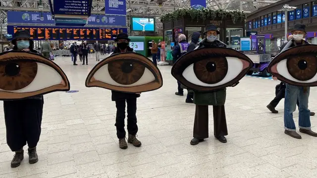 Extinction Rebellion protesters hold pictures of giant eyes at Glasgow Central station