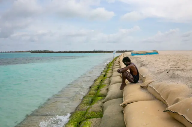 A man sits on a protective sand bag wall on October 10, 2021 in Guraidhoo, Maldives