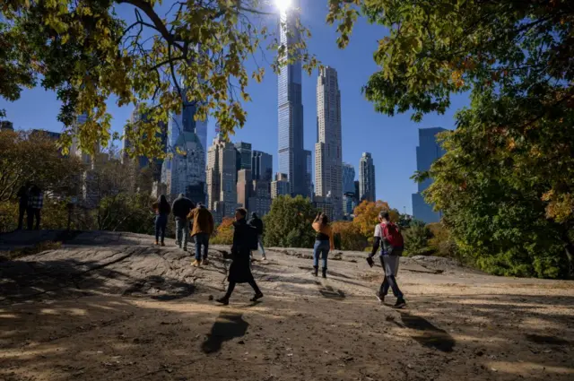 People stand beneath fall foliage and before high-rise buildings of the Manhattan city skyline in Central Park in New York on November 5, 2021