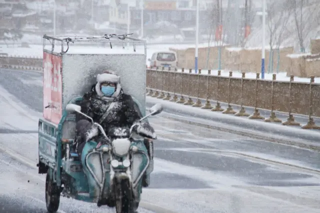 A deliveryman rides an electric tricycle along a road during a heavy snowfall on January 28, 2021 in Weihai, Shandong Province of China.