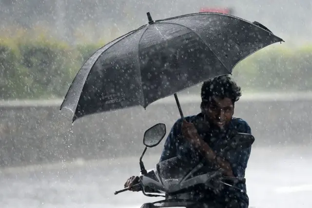 A motorist shelters under an umbrella while riding along a road during heavy monsoon rainfall in Chennai on November 10, 2021.