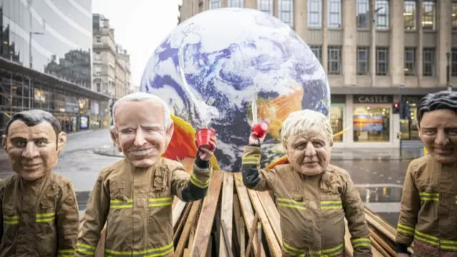 Protesters dressed as world leaders in firefighter uniforms throw water on a papier mache burning globe