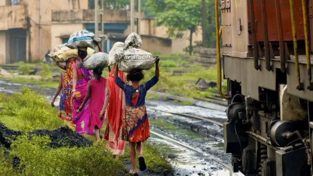 Women carry bag of coal on their heads along a railroad track