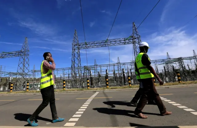 Kenya Electricity Generating Company workers walk past the pylons of high-tension electricity power lines