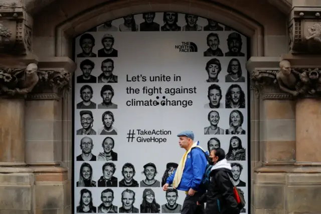 People walk past a North Face banner highlighting climate change in Glasgow