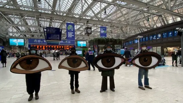 Extinction rebellion protesters hold large eyes at Glasgow central station