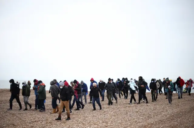 Migrants walk along a beach after being brought ashore by a RNLI Lifeboat, after having crossed the channel, in Dungeness, UK, November 24, 2021.