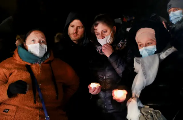 People gather near candles and flowers to pay tribute to the 27 people who died when their dinghy deflated as they attempted to cross the English Channel,