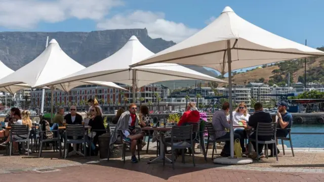 People eating and drinking under umbrellas on the waterfront with a backdrop of Table Mountain