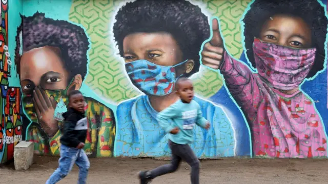 Boys run past a mural of kids in facemasks in South Africa