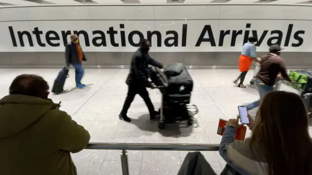 Travellers at airport, next to a sign which says "international arrivals"