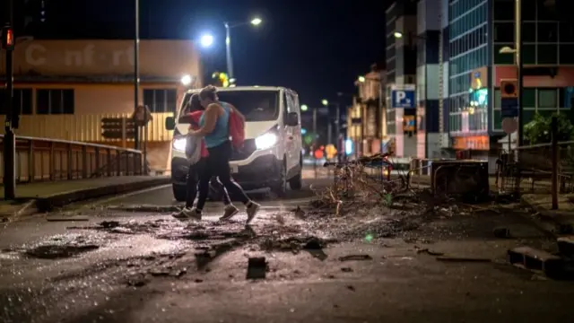 Two women rush to cross a street next to a barricade made of debris after unrest triggered by the coronavirus outbreak curbs