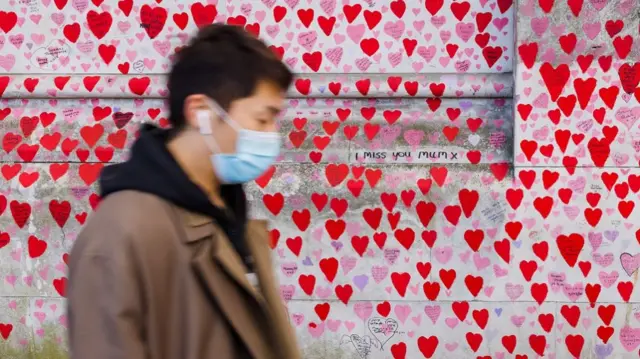 A masked man walks past the Covid memorial wall covered in red hearts