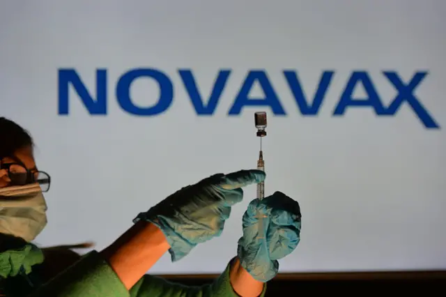 A worker fills a syringe from a vial of Novavax vaccine