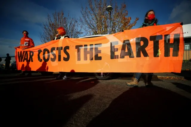 Climate activists in Glasgow hold a banner saying 'War Costs The Earth'