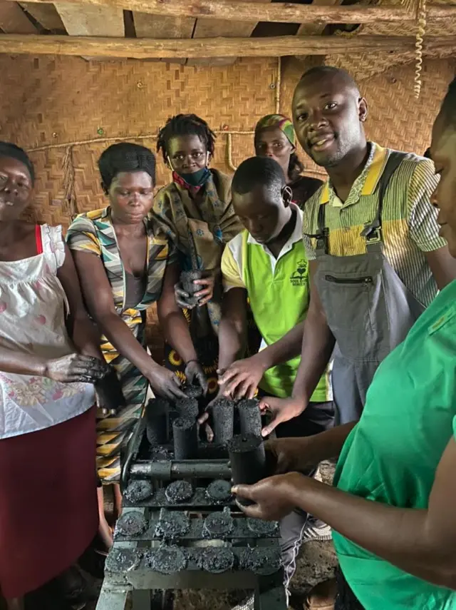 Kakembo Galabuzi Brian (top right, with grey apron) shows how his initiative works