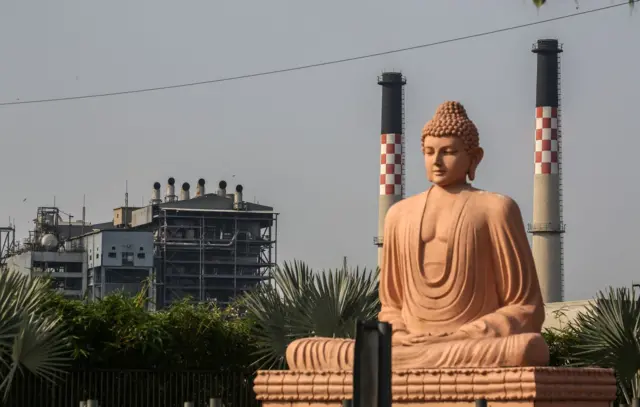 A coal based power station is seen behind a statue of Gautama Buddha