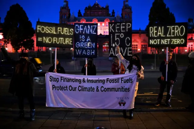 Climate activists hold illuminated signs and a banner protesting against the use of fossil fuels on the sidelines of the COP26 Climate Conference