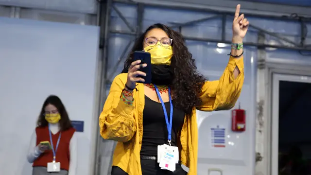 A woman in a yellow face mask at COP26 looks at her phone