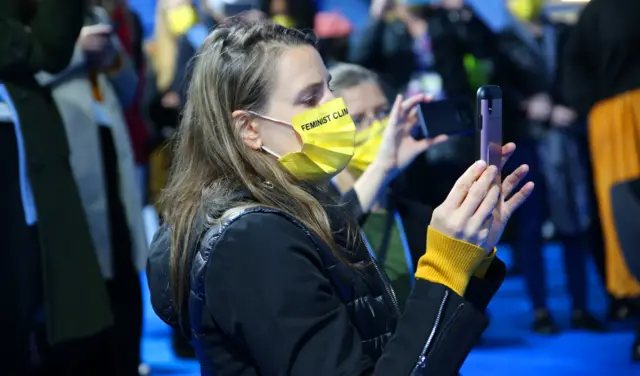 A woman wears a yellow face mask at COP26 looks at her phone