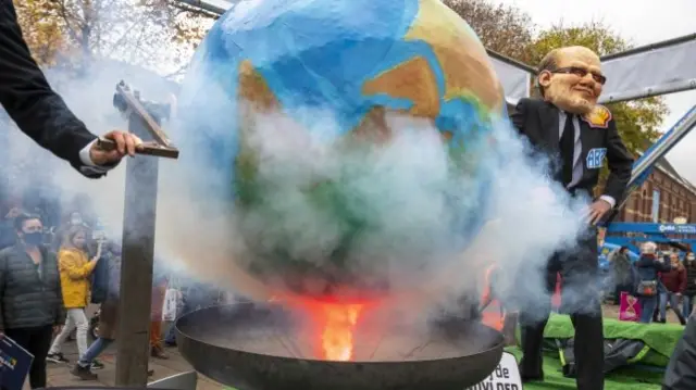 In Amsterdam, the Netherlands, one activist impersonates a Shell oil executive as they turn the crank to heat up the planet