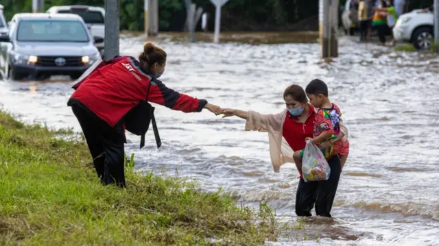 A woman helps another woman and child out of floodwater during flash flooding in Thailand