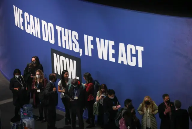 People at COP26 stand in front of a "We can do this if we act now" sign