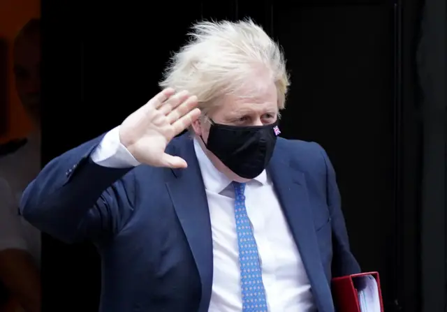 Boris Johnson waving and wearing a mask