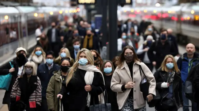 Masked commuters walking along a train platform