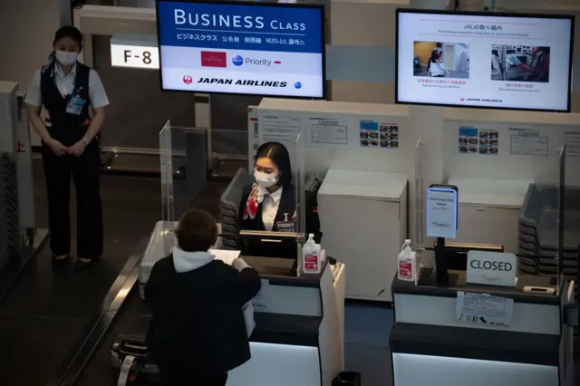 A member of staff assists a passenger at a Japan Airlines business class check-in desk at Haneda Airport