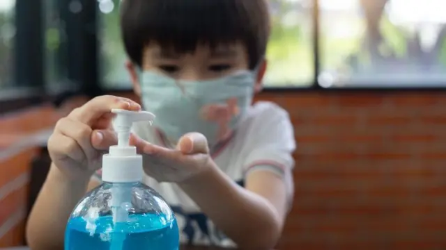 A child in a mask uses hand sanitiser