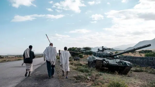 People walk past a military vehicle