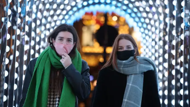 Two women in masks walk through a brightly lit arch