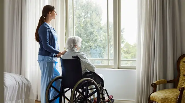 A carer and a woman in a wheelchair look out of a window