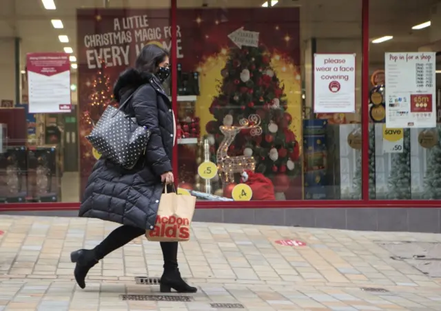 A woman wearing a face mask carries shopping bags