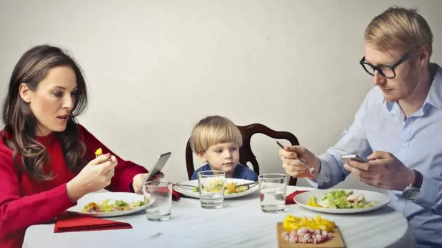 Parents use phones in stock image, as child sits nearby