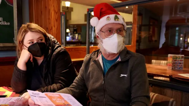 Man wearing mask and Santa hat and his daughter ordering food in a cafe