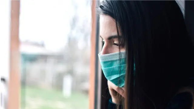 Woman wearing face mask looks out of a window