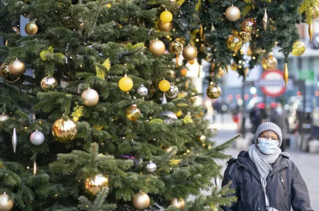 A woman wearing a face mask walks past a Christmas tree in Knightsbridge, London