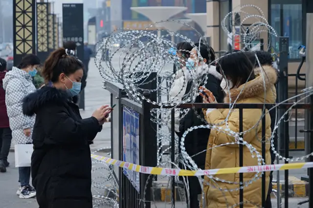 Residents collect daily necessities behind barbed wire installed at the entrance of a community after Xi'an imposed a citywide lockdown