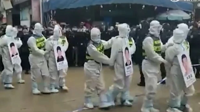 Image of four people in hazmat suits being paraded by police