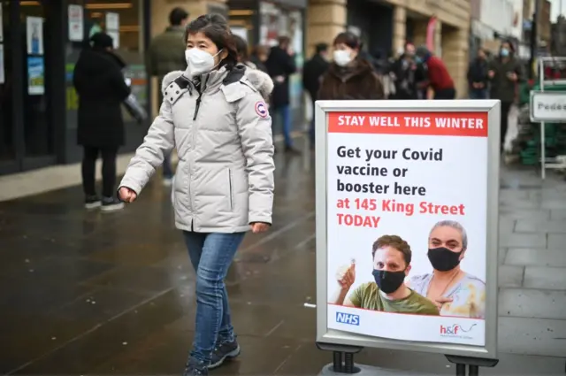 Woman walking past sign promoting booster vaccines