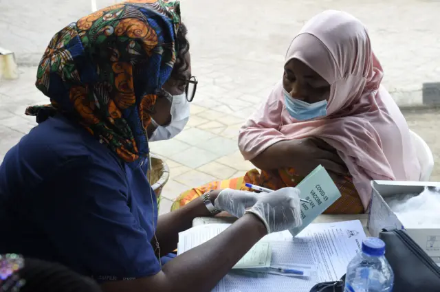 A picture taken on November 26, 2021 shows a health official (L) speaking after administering to a woman a dose of Astrazeneca's Vaxzevria Covid-19 vaccine in Lagos